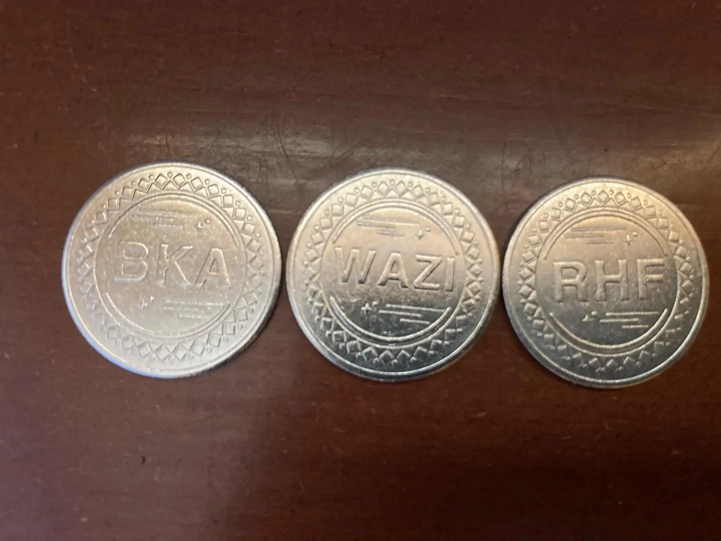 Three metal tokens from Wazi and its partners lie side by side on a dark table.
