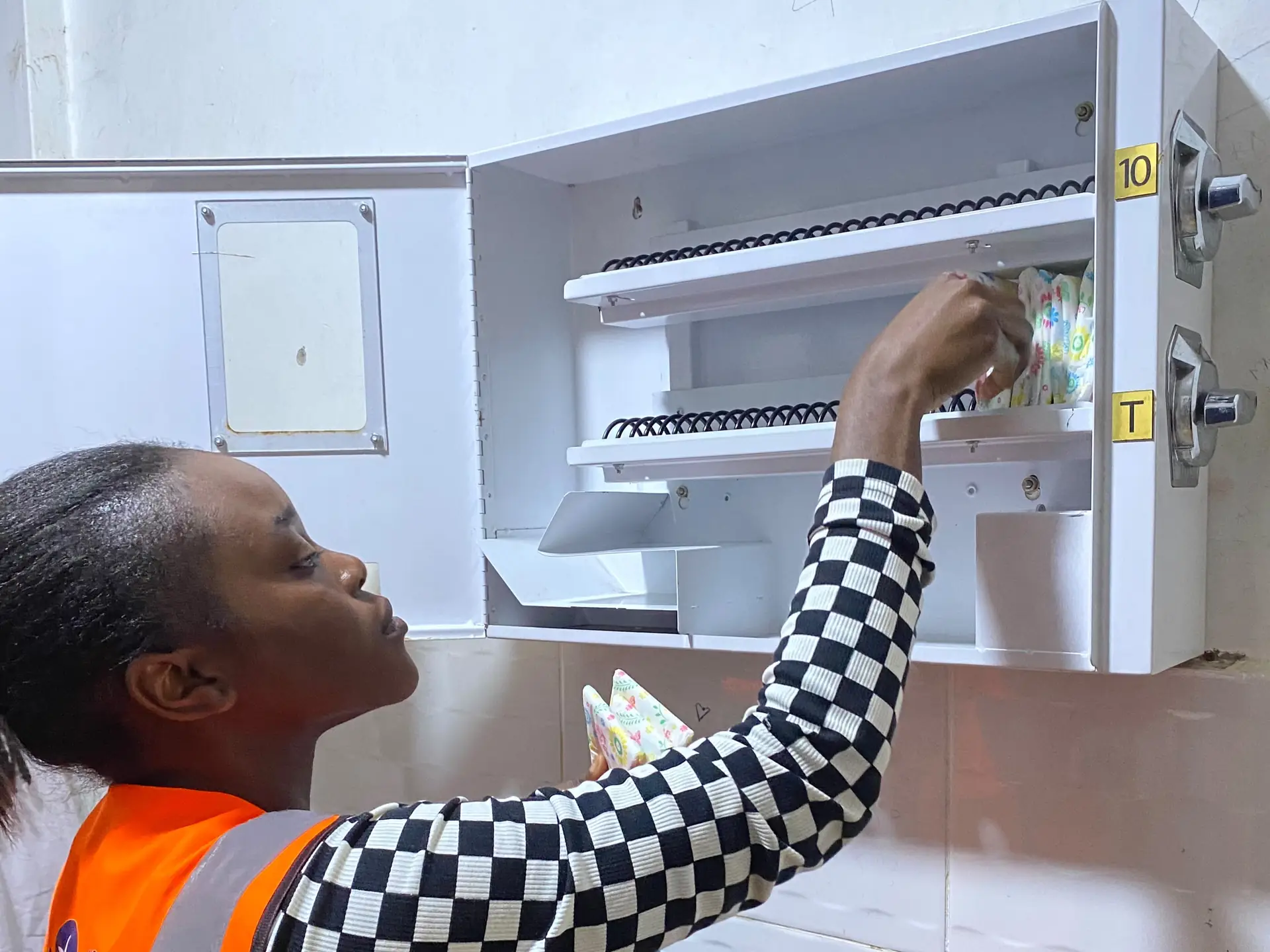 A volunteer reaches up to stock the coils of an open wall dispenser.