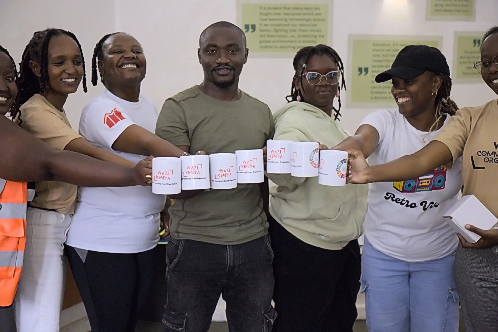 Wazi members reach forward to toast with their branded mugs, smiling together.
